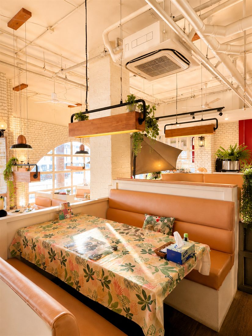 Booth seating with floral tablecloths under copper pendant planters